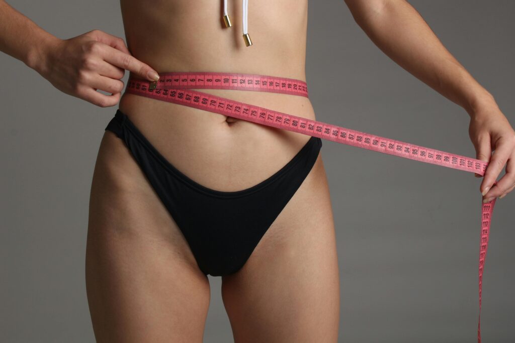 TESTIMONIOS Close-up of a woman measuring her waist with a pink tape, symbolizing fitness and health.