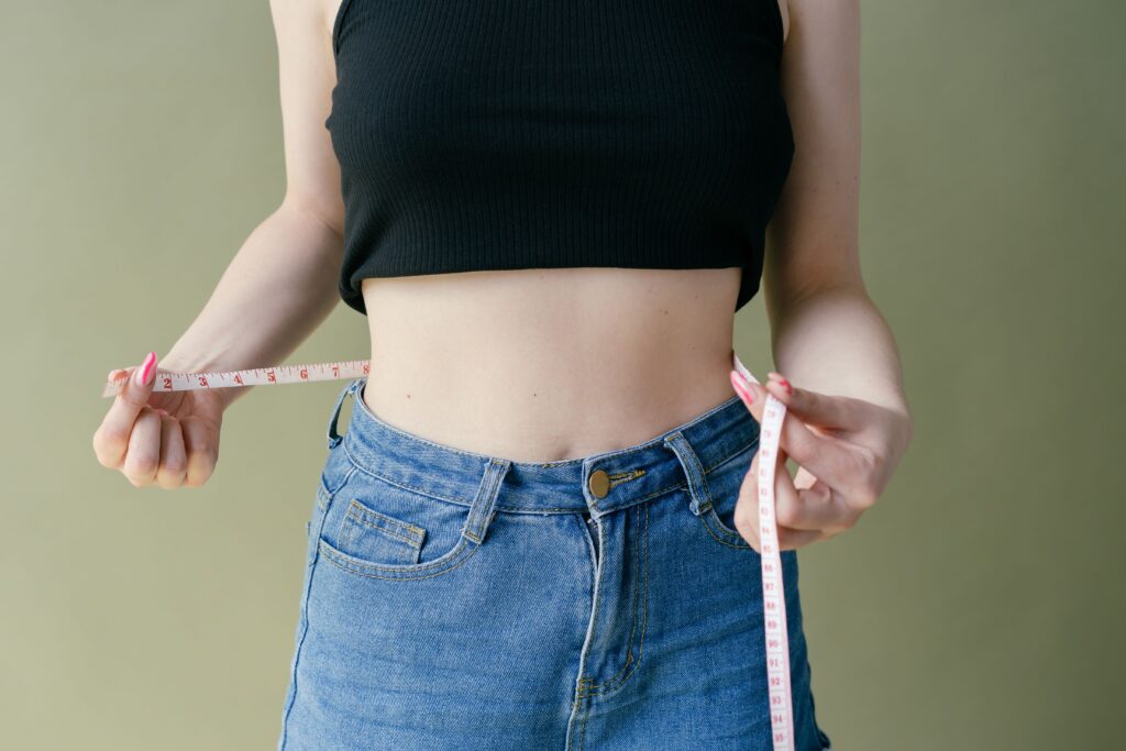 TESTIMONIOS A woman in denim and crop top using measuring tape for waist check.